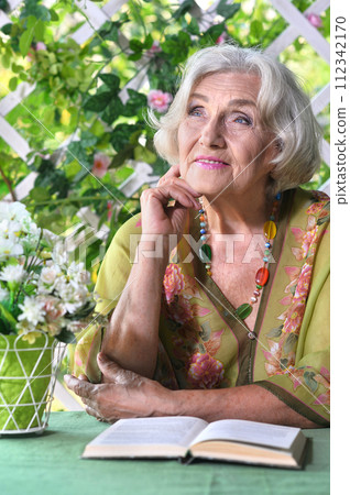 Beautiful elderly woman sits at a table and reading book 112342170