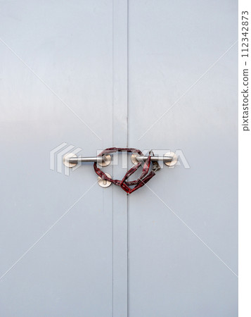 Closeup of the metal door handle locked with chain and paddle. Closeup of the metal door handle locked with chain and paddle. 112342873