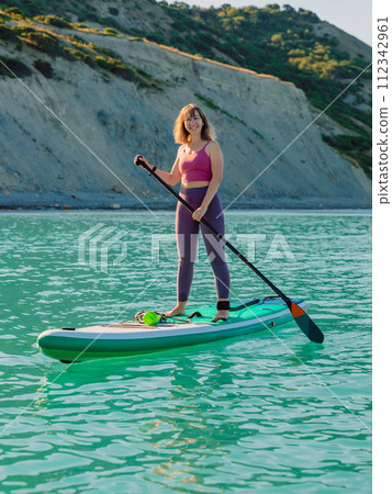Smiling woman on stand up paddle board at sea. Woman on SUP board in sea. Smiling woman on stand up paddle board at sea. Woman on SUP board in sea. 112342961