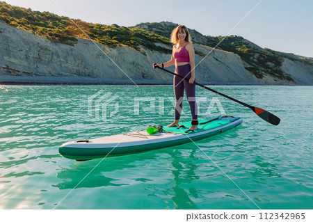 Smiling woman on stand up paddle board at sea. Woman on SUP board in sea. 112342965