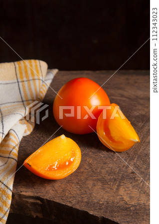 Cut and whole of yellow tomato and yellow towel on wooden background.. Cut and whole of yellow tomato and yellow towel on wooden background.. 112343023