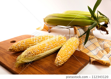 Cutting board with three cobs sweet corn on white wooden background.. 112343120