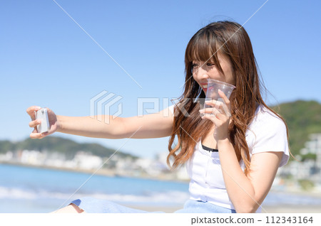 A woman taking a picture with a smartphone while holding a drink A woman taking a picture with a smartphone while holding a drink 112343164
