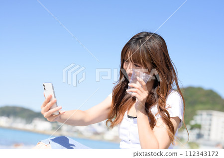 A woman taking a picture with a smartphone while holding a drink A woman taking a picture with a smartphone while holding a drink 112343172