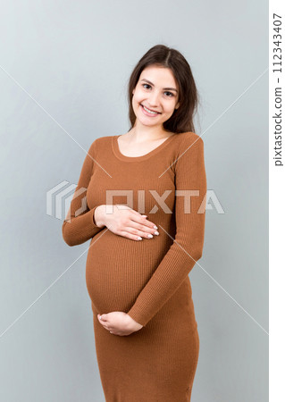 Happy pregnant woman touching her abdomen at Colored background. Future mother. Expecting of a baby. Copy space 112343407