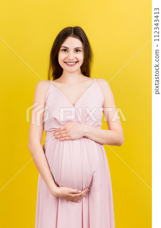 Happy pregnant woman touching her abdomen at Colored background. Future mother. Expecting of a baby. Copy space Happy pregnant woman touching her abdomen at Colored background. Future mother. Expecting of a baby. Copy space 112343413