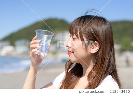 Woman resting on the sandy beach with a drink in hand 112343420