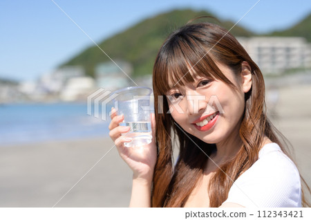 Woman resting on the sandy beach with a drink in hand 112343421