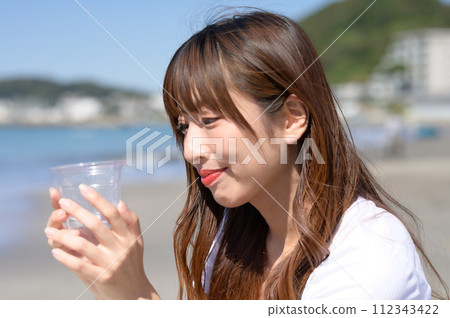 Woman resting on the sandy beach with a drink in hand 112343422