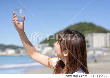 Woman resting on the sandy beach with a drink in hand Woman resting on the sandy beach with a drink in hand 112343427
