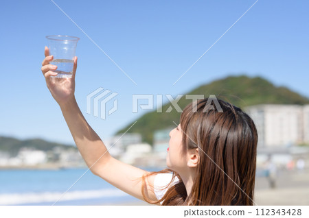 Woman resting on the sandy beach with a drink in hand 112343428