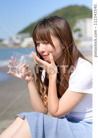 Woman resting on the sandy beach with a drink in hand Woman resting on the sandy beach with a drink in hand 112343540
