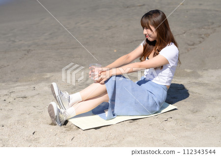 Woman resting on the sandy beach with a drink in hand 112343544