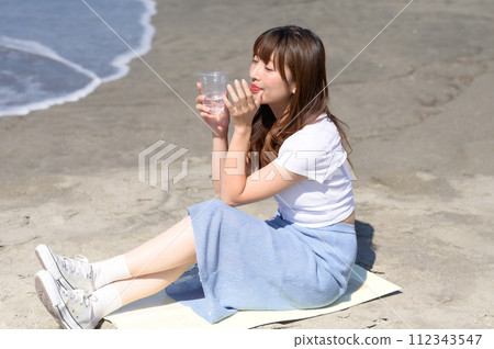 Woman resting on the sandy beach with a drink in hand Woman resting on the sandy beach with a drink in hand 112343547