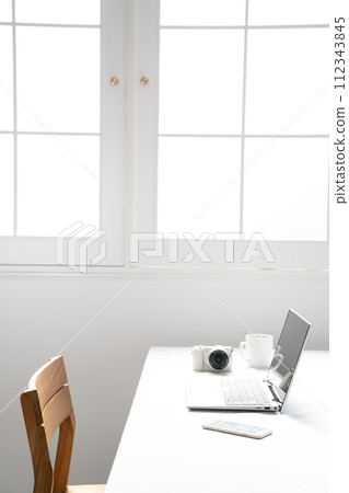 Image with a laptop and digital camera next to a white window 112343845