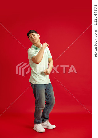 Happy, joyful man, student in denim jeans and T-shirt dancing in motion against red studio background. Success. 112344872