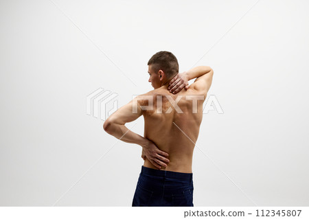Healthy spine. Rear view of shirtless young man with relief strong back standing in jeans isolated over white studio background Healthy spine. Rear view of shirtless young man with relief strong back standing in jeans isolated over white studio background 112345807