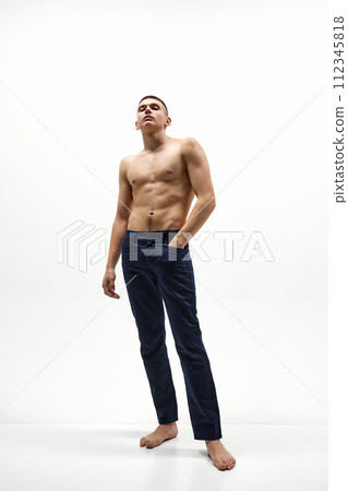 Full-length image of handsome, confident, shirtless man with muscular body posing in jeans isolated over white studio background 112345818