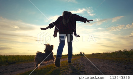 child girl running with a dog in the park. happy family freedom a kid dream concept. silhouette of a child girl running along the road in the park at sunset view from the back with a shaggy sun dog child girl running with a dog in the park. happy family freedom a kid dream concept. silhouette of a child girl running along the road in the park at sunset view from the back with a shaggy sun dog 112345826