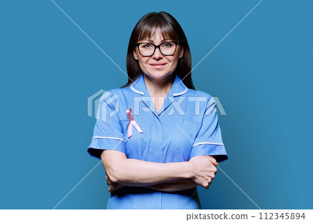 Smiling female nurse in blue uniform with pink ribbon, on blue background Smiling female nurse in blue uniform with pink ribbon, on blue background 112345894