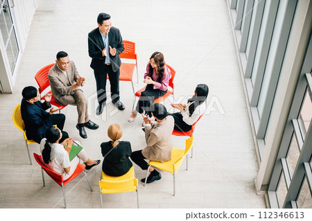 Top view captures a diverse group in a busy office, collaborating and engaged in discussions. A businessman and businesswoman sit at a conference, allowing for your business meeting concept. Top view captures a diverse group in a busy office, collaborating and engaged in discussions. A businessman and businesswoman sit at a conference, allowing for your business meeting concept. 112346613