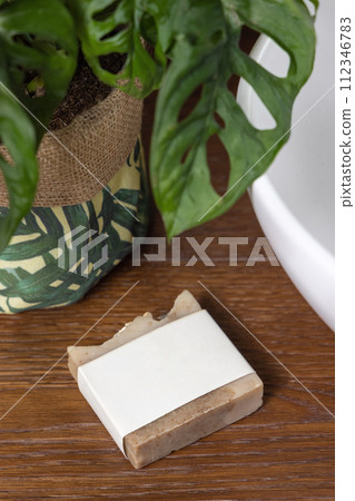 Soap bar with blank label on bath wooden countertop near monstera plant close up, mockup 112346783