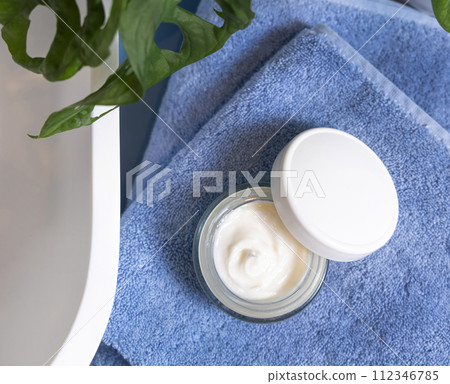 Opened cream jar on blue towels near basin and green monstera in bath, lid mockup 112346785