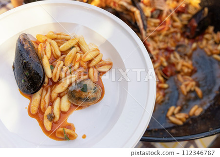 Plastic plate of pasta with black mussels, shrimps and tomatoes while it is served close up 112346787