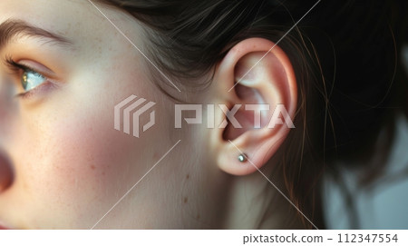 Close-up of a young womans ear with a beautiful silver earring, showcasing elegance and style. Close-up of a young womans ear with a beautiful silver earring, showcasing elegance and style. 112347554