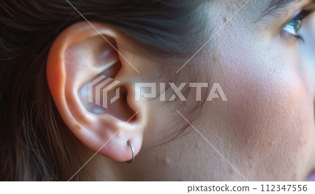 Closeup of a elegant womans ear with a stylish silver hoop earring in natural light. Closeup of a elegant womans ear with a stylish silver hoop earring in natural light. 112347556