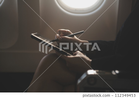 Blonde female tourist checking incoming notification on smartphone sitting on seat of airplane with netbook.Young businesswoman share media from telephone on laptop computer during plane flight Blonde female tourist checking incoming notification on smartphone sitting on seat of airplane with netbook.Young businesswoman share media from telephone on laptop computer during plane flight 112349453