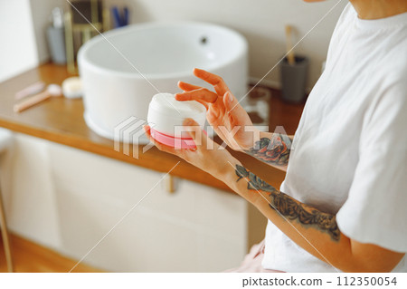 Close up of woman opening jar with face cream while standing in bathroom. High quality photo 112350054