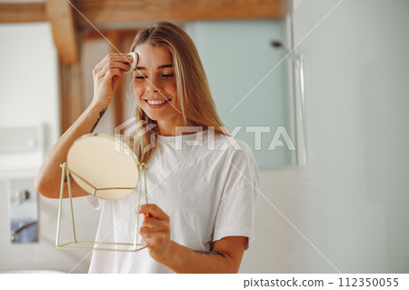 Smiling woman wiping her face with cotton pad in the bathroom. Skin care concept 112350055