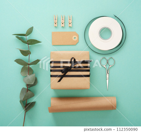 Summer gift wrapping. Brown craft wrapping paper, black ribbon, scissors, eucalyptus, tags. Mint background. 112350090