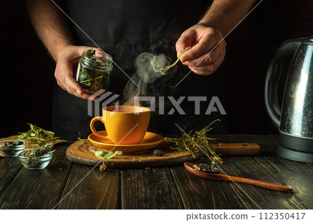 A man adds motherwort to a mug of boiling water to make a soothing tea. Traditional medicine concept or making medicinal tea. Treating the flu virus at home A man adds motherwort to a mug of boiling water to make a soothing tea. Traditional medicine concept or making medicinal tea. Treating the flu virus at home 112350417