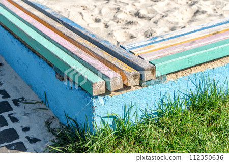 Concrete barrier with colorful wooden bars serving as seats, surrounding a children's sandbox 112350636