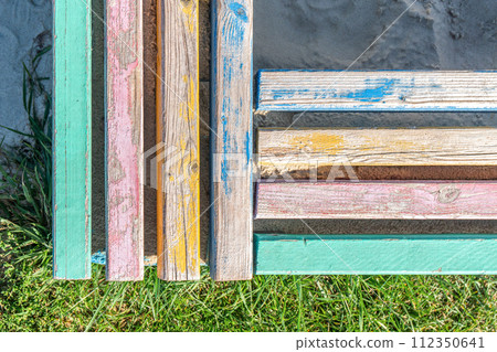 Concrete barrier with colorful wooden bars serving as seats, surrounding a children's sandbox Concrete barrier with colorful wooden bars serving as seats, surrounding a children's sandbox 112350641