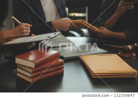 Justice and Law concept. Legal counsel presents to the client a signed contract with gavel and legal law or legal having team meeting at law firm in background 112350647