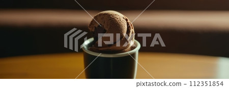 Delicious cup of ice cream sits on table in front of window, basking in natural light. For advertising, banner, relaxation, lifestyle, menu, food, dessert, culinary or cafe themed content. Copy space. Delicious cup of ice cream sits on table in front of window, basking in natural light. For advertising, banner, relaxation, lifestyle, menu, food, dessert, culinary or cafe themed content. Copy space. 112351854