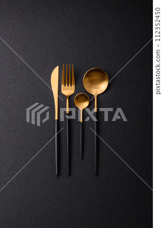 Cutlery fork, knife and spoon on a dark textured concrete background Cutlery fork, knife and spoon on a dark textured concrete background 112352450