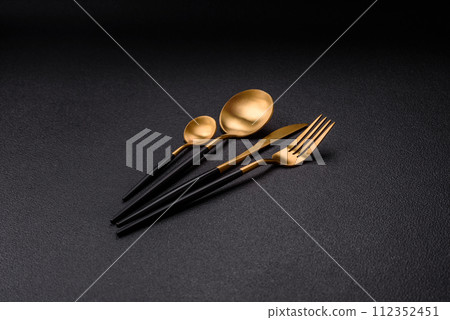 Cutlery fork, knife and spoon on a dark textured concrete background Cutlery fork, knife and spoon on a dark textured concrete background 112352451