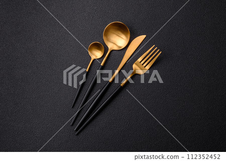 Cutlery fork, knife and spoon on a dark textured concrete background Cutlery fork, knife and spoon on a dark textured concrete background 112352452
