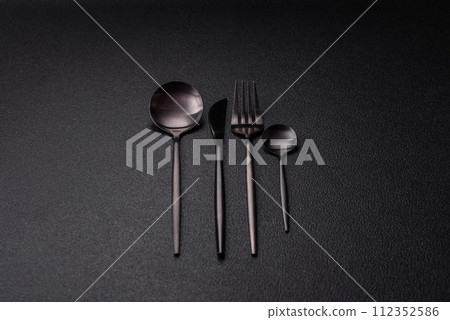 Cutlery fork, knife and spoon on a dark textured concrete background Cutlery fork, knife and spoon on a dark textured concrete background 112352586