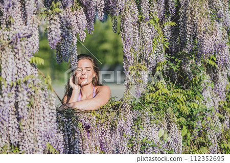 Woman wisteria lilac dress. Thoughtful happy mature woman in purple dress surrounded by chinese wisteria Woman wisteria lilac dress. Thoughtful happy mature woman in purple dress surrounded by chinese wisteria 112352695