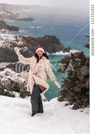 Outdoor winter portrait of happy smiling woman, light faux fur coat holding heart sparkler, posing against sea and snow background Outdoor winter portrait of happy smiling woman, light faux fur coat holding heart sparkler, posing against sea and snow background 112352852