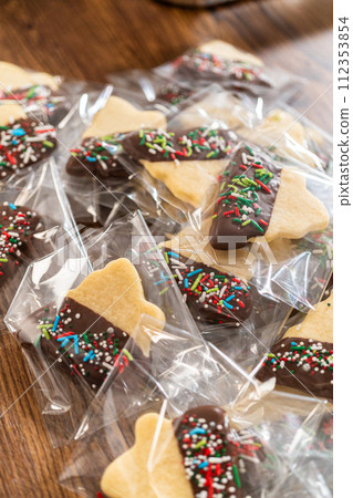 Carefully packaging Christmas cutout cookies, half-dipped in chocolate and presented in clear cellophane wrapping, perfect for festive gifting. 112353854
