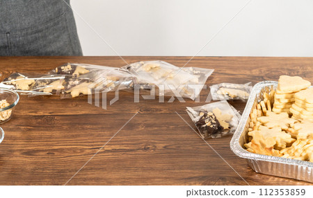 Carefully packaging Christmas cutout cookies, half-dipped in chocolate and presented in clear cellophane wrapping, perfect for festive gifting. 112353859