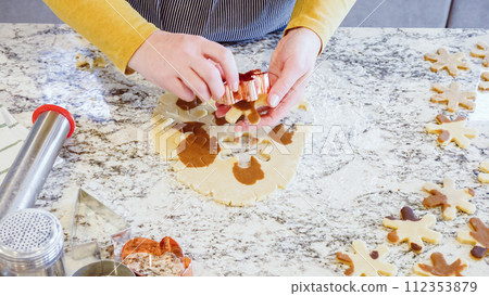 Using various festive cookie cutters, we're cutting out charming gingerbread cookies from the rolled dough on the sleek marble counter, bringing holiday cheer to the modern kitchen. Using various festive cookie cutters, we're cutting out charming gingerbread cookies from the rolled dough on the sleek marble counter, bringing holiday cheer to the modern kitchen. 112353879