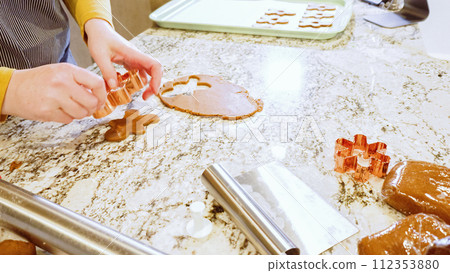 Using various festive cookie cutters, we're cutting out charming gingerbread cookies from the rolled dough on the sleek marble counter, bringing holiday cheer to the modern kitchen. 112353880