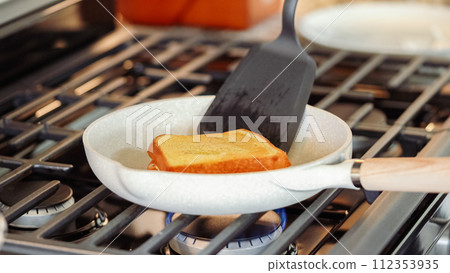 Within the sleek setting of a modern white kitchen, banana slices and brioche bread sizzle on a non-stick pan over a gas stove, setting the stage for an enticing grilled peanut butter banana sandwich. Within the sleek setting of a modern white kitchen, banana slices and brioche bread sizzle on a non-stick pan over a gas stove, setting the stage for an enticing grilled peanut butter banana sandwich. 112353935
